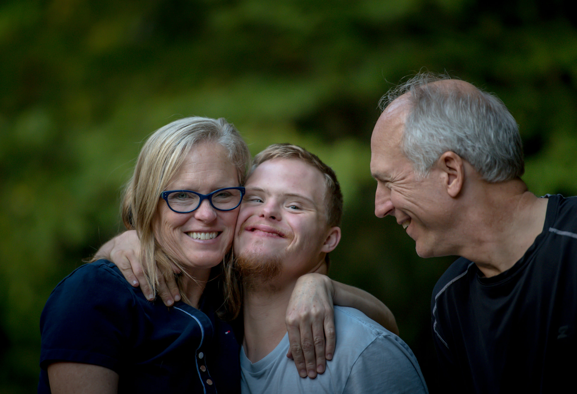 Mother, son with Down syndrome, and father smiling together outdoors