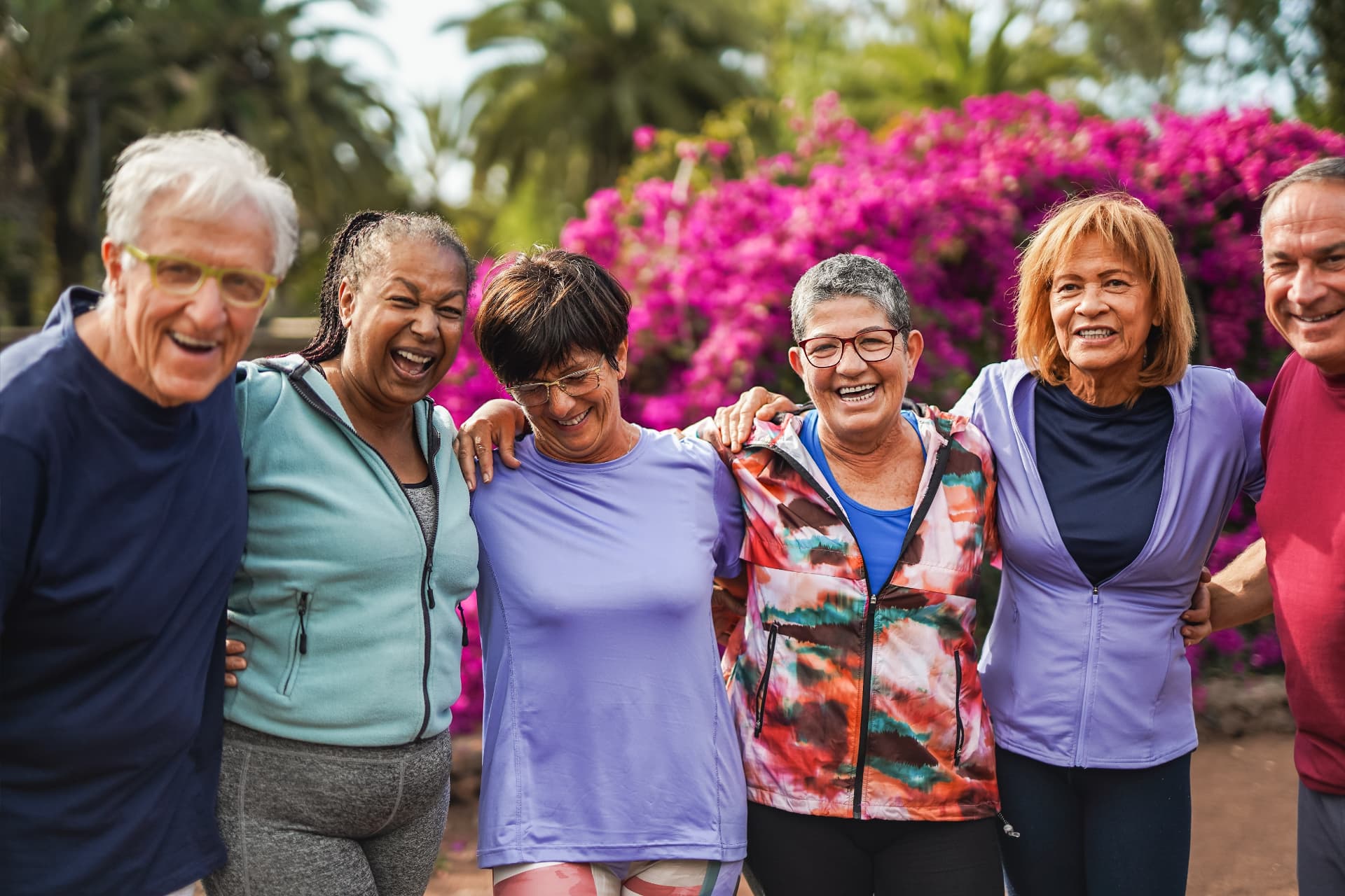 Group of smiling older adults embracing outdoors in a park after exercising together